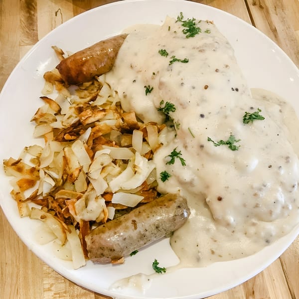 Biscuits and gravy with two sausages and crispy home fries on a white plate.