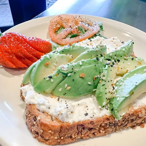 Avocado toast with cream cheese, everything bagel seasoning, a strawberry, and tomato on a white plate.