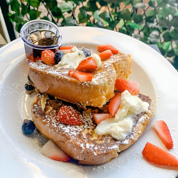Thick-cut French toast topped with strawberries, blueberries, whipped cream, powdered sugar, and a side of syrup.